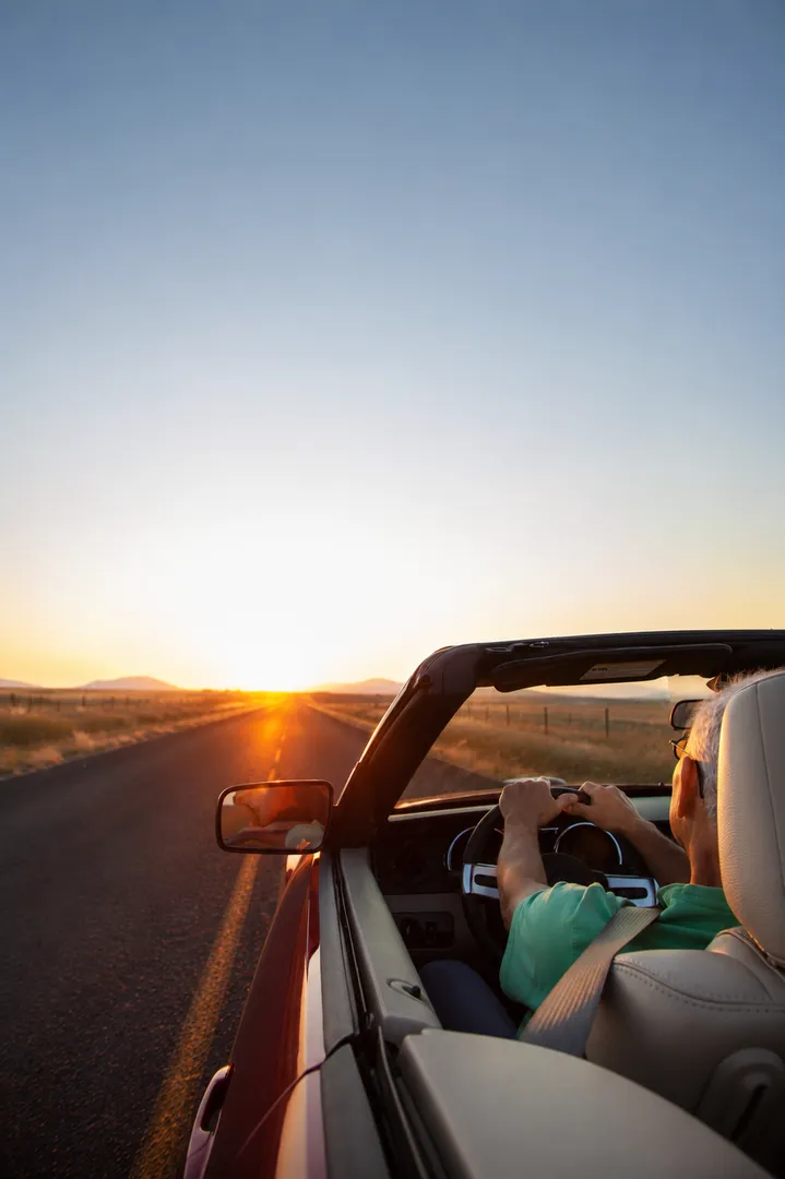 Mann fährt bei Sonnenuntergang in einem Cabriolet über eine Landstraße